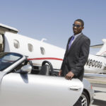 African-American businessman opening door of convertible on landing strip.